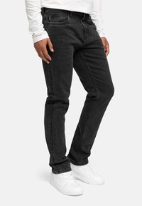 Sorte denimjeans med slim fit, middels høy midje, fem-lomme design og kontrasterende sømmer. Kombinert med hvite sneakers.