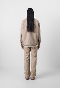 Veste oversize beige avec une texture lisse, associée à un pantalon beige ample. La tenue présente un design minimaliste.