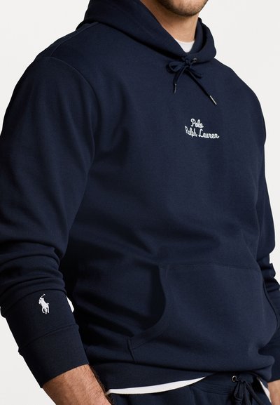 Tamsiai mėlyna džemperis su gobtuvu, pagamintas iš minkštos medžiagos, su siuvinėta logotipu krūtinėje ir mažu logotipu ant rankovės, priekinė kišenė ir raištelio gobtuvas.