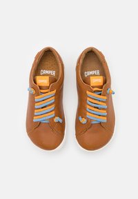Sneakers in pelle marrone con lacci blu e arancioni, punta tonda, suola in gomma bianca e un'etichetta del logo Camper sulla linguetta.
