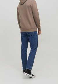 Sudadera caqui de corte relajado, combinada con jeans de mezclilla azul y zapatillas negras. El conjunto presenta un tejido texturizado y un diseño casual.