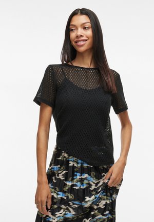 Top negru tricotat cu un design din plasă, cu mâneci scurte și guler rotund, asociat cu o fustă patterned în nuanțe de albastru și verde.