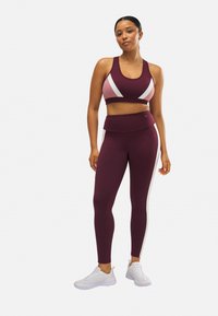 Conjunto deportivo en color burdeos que incluye una camiseta corta con acentos en blanco y rosa, leggins de cintura alta con franjas laterales, acompañado de zapatillas blancas.