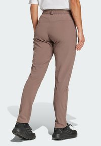 Brune tights med elastisk midje, med innsvingte ben og sidelommer. Kombinert med sorte sportssko.
