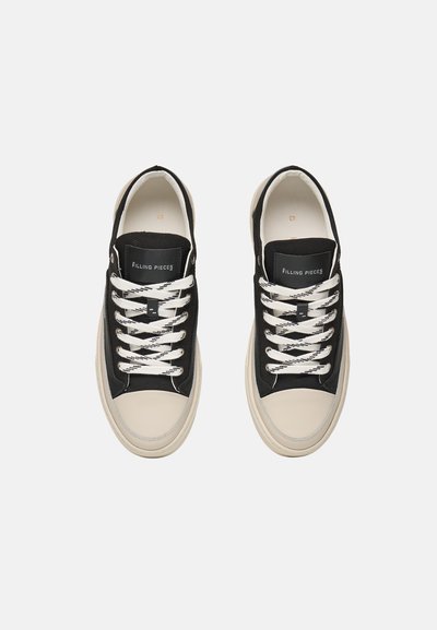 Para czarnych i beżowych sneakersów z białymi i czarnymi sznurowadłami, widziana z góry na jednolitym jasnym tle.