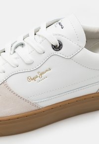 Baskets en cuir blanc avec bout en daim beige, semelle gomme, lacets blancs et logo doré "Pepe Jeans London" sur le côté.