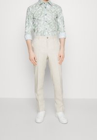 Lichtgroen shirt met palmbladenpatroon en opgerolde mouwen, gecombineerd met beige linnen broek en witte sneakers. Flat front ontwerp, casual fit.