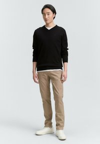 Zwarte V-hals trui over een wit shirt, gecombineerd met tan chinos en witte sneakers. De trui heeft geribbelde boorden en een slimfit ontwerp.