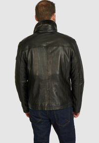 Chaqueta de cuero negra con un cuello alto, costuras visibles y una textura suave. Combinada con jeans oscuros, vista desde atrás.