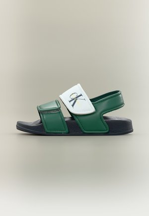 Sandalo sportivo verde e blu navy con due cinturini regolabili, uno dei cinturini bianchi con il logo Calvin Klein, su sfondo neutro.