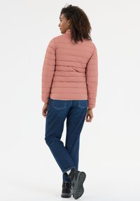Pink pufferjakke med vandret syninger, høj krave og en glat tekstur, båret med blå jeans og sorte støvler, set bagfra.