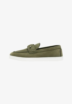 Mocasín verde oliva tipo slip-on con suela de goma blanca y detalle decorativo de tira sobre la parte superior, visto de lado.