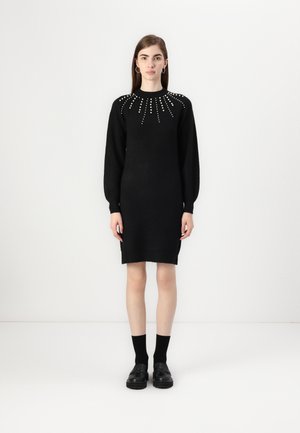 Abito nero a maglia con lunghe maniche a palloncino, decorato con borchie metalliche in un motivo radiante attorno al colletto, silhouette aderente.