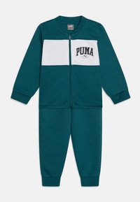 Chándal de color aguamarina con un panel horizontal blanco, que incluye una chaqueta con cremallera y pantalones a juego, fabricado en una tela suave, con un logo impreso.