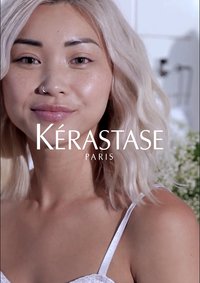 Il branding di Kérastase in bold bianco su una donna con capelli platino ondulati fino alle spalle, che indossa un top leggero, su uno sfondo morbido.