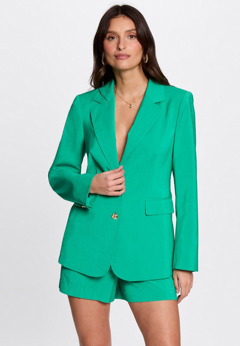 Groene blazer van een lichtgewicht stof met een getailleerde pasvorm, met uitgesneden revers, dubbele knopen en zijzakken. Gecombineerd met bijpassende shorts.