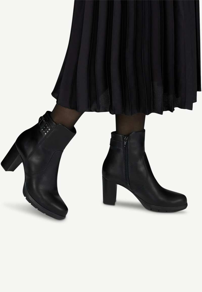 Bottes cheville en cuir noir à talons blocs portées avec des collants noirs transparents et une jupe midi plissée.