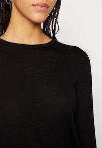 Czarny sweter dziany z okrągłym dekoltem, miękką fakturą i dopasowanym krojem. Materiał wydaje się lekki i lekko prześwitujący.