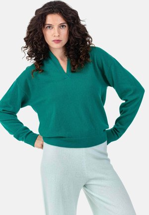 Pull en maille vert avec un col en V et une coupe décontractée. Associé à un pantalon ajusté de couleur menthe claire. Texture douce, style décontracté.