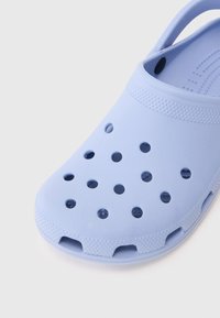 Svijetloplavi gumeni klompa s ventilacijskim rupama i teksturiranim remenom na jednostavnoj bijeloj pozadini.