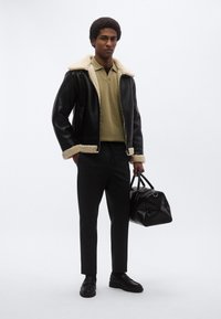 Μαύρο δερμάτινο μπουφάν με επένδυση από shearling, χακί πόλο, σκούροι παντελόνια και μαύρη τσάντα με υφή. Ολοκληρώνουν το σύνολο λουστρινένια δερμάτινα παπούτσια.