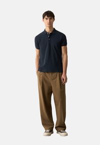 Polo shirt blu navy con colletto classico e tre bottoni, abbinato a pantaloni a vita alta marrone chiaro, indossato con sneakers bianche.