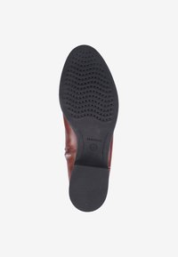 Bruine leren schoen met een lage hak, gestructureerde rubberen zool met cirkel- en golfpatronen, en een uitgesproken merkimpressie op de zool.