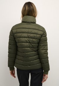 Olijfgroene pufferjack met een hoge kraag, gestikte desig en geribde boorden. Zachte textuur en getailleerde silhouet.
