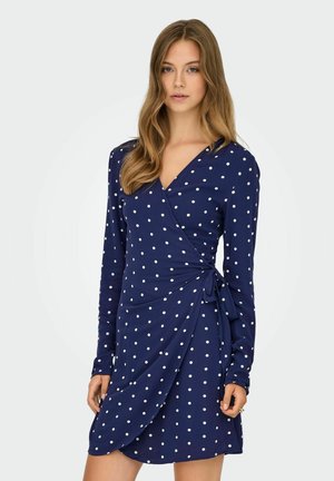 Navy wrap dress made of soft fabric, featuring white polka dots, long sleeves, and a tie detail at the waist with a flattering silhouette.