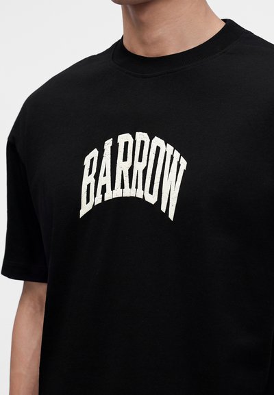 Άτομο που φοράει μαύρη μπλούζα με τη λέξη "BARROW" τυπωμένη σε μεγάλα λευκά καμπυλωτά γράμματα στο στήθος.