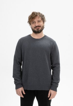 Un pull-over gris foncé à col rond avec des manches longues, des poignets et un ourlet côtelés, fabriqué dans un tissu texturé, porté sur un pantalon noir.