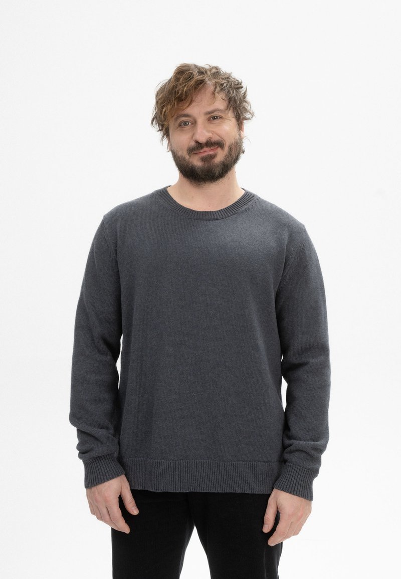 Dunkelgrauer Rundhalsausschnitt-Pullover mit langen Ärmeln, gerippten Bündchen und Saum, aus einem strukturierten Stoff, getragen über schwarzen Hosen.