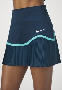 Falda deportiva azul marino con diseño plisado, ribete turquesa y logo blanco de Nike. Confeccionada con un material liso y elástico para mayor comodidad.