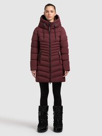 Giacca a piumino color marrone scuro con cappuccio alto, chiusura con zip e cuciture a chevron. Abbinata a stivali da neve neri con lacci elastici e drappeggio.