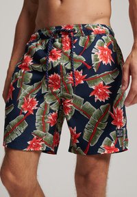Pantaloni da bagno da uomo con uno sfondo blu navy scuro, caratterizzati da un motivo floreale tropicale in rosso e verde. Vita elasticizzata con dettaglio di cordino.