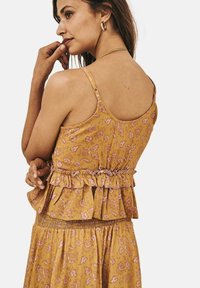 Camiseta sin mangas de patrón floral amarillo con dobladillo con volantes, tirantes ajustables y cintura fruncida. Tejido suave con delicados acentos rosas.