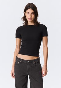 Black fitted short-sleeve top with a round neckline, made from smooth material. Paired with high-waisted dark jeans featuring copper hardware.