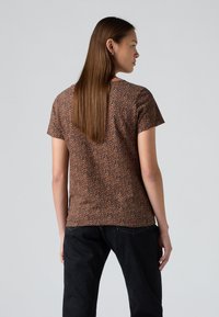 Brun t-skjorte med en subtil dyreprint, korte ermer og rund hals, kombinert med svarte høy midje jeans.
