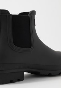 Black rubber ankle boot with elastic side panels, textured sole, smooth upper, and signature accent.