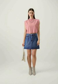 Top court rose, jupe en denim bleue en forme de A, bottines grises, et sac à main beige clair. Fond lumineux, design minimaliste, style décontracté.