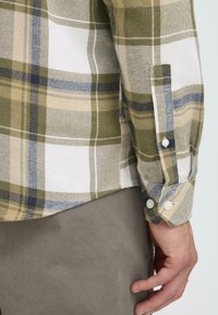 Groene, beige en blauwe geruite shirt met een gestructureerde stof; beschikt over knoopsluitingen bij de mouwen en een gebogen zoom. Draag het met grijze broek.