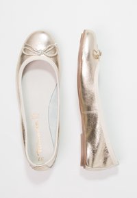 Gouden metallic ballerina's met een afgeronde neus, een decoratieve strik op de neus en een contrasterende crèmekleurige elastische rand. Glad oppervlak.