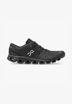 Zapatilla de correr negra y ligera con parte superior de malla, suela segmentada distintiva, cierre de cordones y logotipo reflectante en el lateral y el talón.