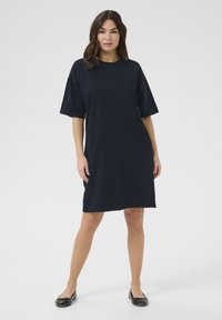 Navy blue, short-sleeve cotton dress with a relaxed fit, round neckline, and a knee-length hem. Worn with black flat shoes.