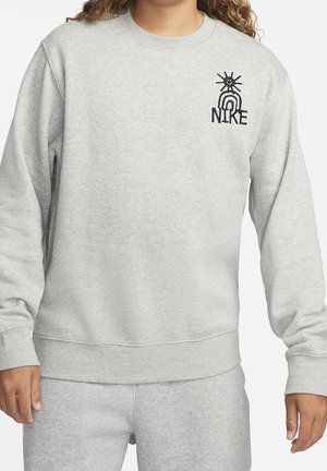 Osoba nosi jasnoszarą bluzę z czarnym logo Nike, wzorem słońca i tęczy na piersi, w połączeniu z dopasowanymi szarymi spodniami.