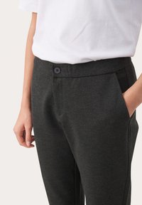 Donkergrijze op maat gemaakte broeken met een gladde textuur, voorzien van een knoopsluiting en zijzakken. Gepaard met een witte t-shirt met ronde hals.