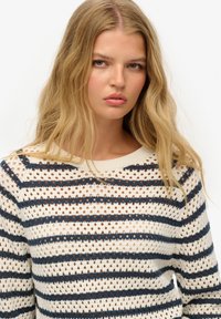 Pull en tricot avec une base crème, mettant en avant des rayures verticales bleu marine et rouille, un design de points ouverts et un col rond.