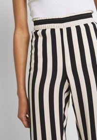 Zwart en crème gestreepte broek met een brede elastische tailleband, een gladde textuur en een aangesloten ontwerp van de taille tot de enkels.