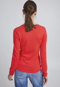 Pull rouge à manches longues en tissu tricoté lisse avec un col rond et un ourlet côtelé, associé à un jean en denim bleu clair.
