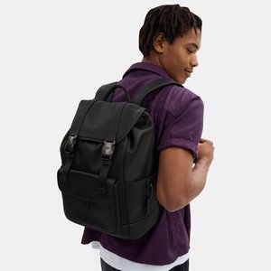 Mladić u ljubičastoj košulji nosi crni kožni ruksak s prednjim kopčama i bočnim džepom na patent.